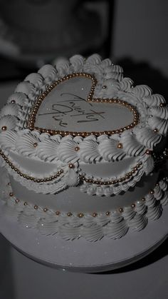 a wedding cake with white frosting and gold decorations on it's sides, topped with a heart - shaped decoration