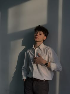 a young man standing in front of a wall with his hands on his hips, wearing a white shirt and tie