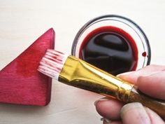 a hand holding a paintbrush with red liquid in it and an arrow on the table