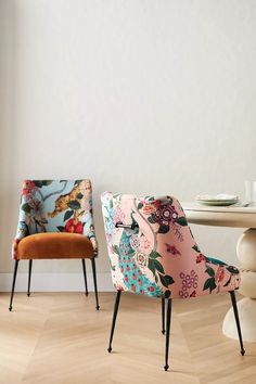 two colorful chairs sitting next to each other on top of a hard wood floor in front of a white wall