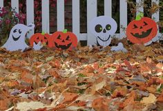 three halloween pumpkins with faces on them in front of a white picket fence and flowers