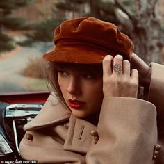 a woman wearing a brown hat and trench coat holding her hand up to her head