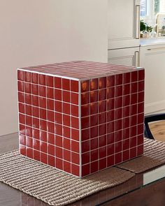 a red square shaped object sitting on top of a wooden table next to a window