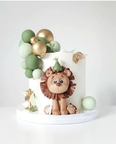 a white cake with a lion on top and green balloons around the edges, sitting on a table