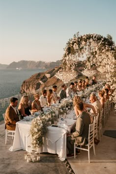 a group of people sitting around a table with white clothed tables and flowers on it