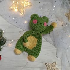 a crocheted frog sitting on top of a table next to christmas decorations and lights