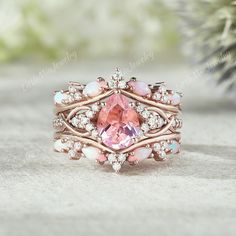 a ring with pink stones and white diamonds on the side, sitting next to a pine tree