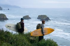 two surfers are looking out at the ocean with their surfboards in hand,