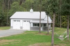 a white house with a hammock in the front yard and trees around it