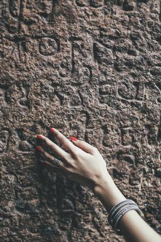 a woman's hand with red nail polish on her nails next to a stone wall