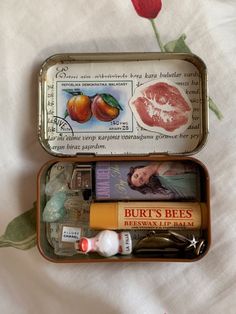 an open tin box containing lip balm, lipstick, and various other items on a bed