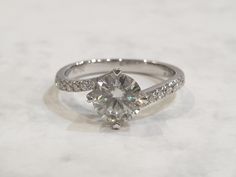 a white gold ring with diamonds on top and side stones around the band, sitting on a marble surface