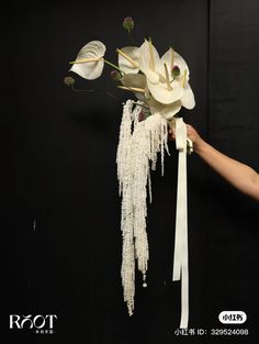 a person holding a bouquet of flowers with long white ribbons on it's side