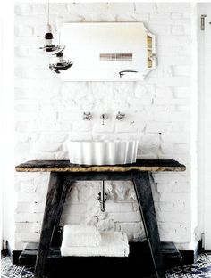 a white brick wall with two sinks and a wooden table in front of the mirror