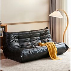 a black leather futon couch with a yellow blanket on it in front of a window