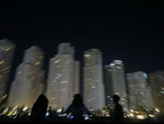 two people are standing in front of some tall buildings at night with the lights on