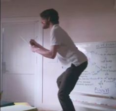 a man standing in front of a whiteboard while holding a piece of paper with writing on it