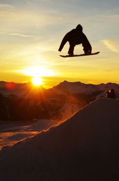 a man flying through the air while riding a snowboard in front of a sunset