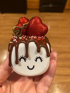 a hand holding a small chocolate dessert with two hearts on top