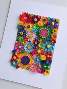 an art piece made out of paper with colorful flowers on the bottom and center, surrounded by smaller cut outs