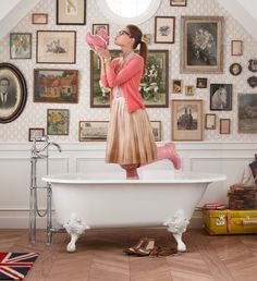 a woman standing in front of a bathtub with pink shoes on the floor and her feet up