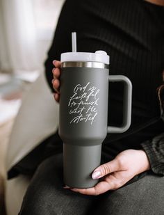 a woman holding a gray coffee cup with writing on the side and a straw in her hand