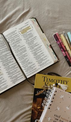 an open book on a bed next to some pens and books with writing in them