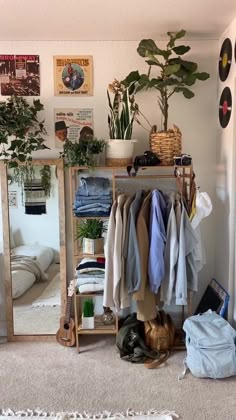 a room filled with clothes and plants next to a mirror on the wall above it