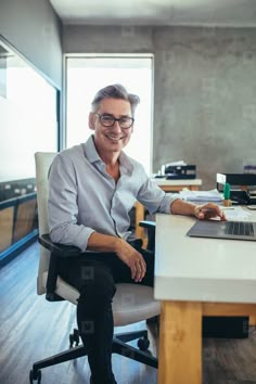 a man sitting at a desk with a laptop computer in front of him and smiling