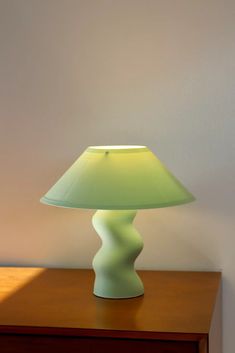 a green lamp sitting on top of a wooden table next to a white wall and brown dresser