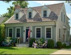 a white house with a flag on the front porch and flowers in the front yard