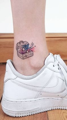 a small tattoo on the ankle of a woman's foot, with an open suitcase