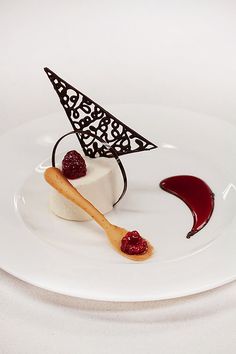 a white plate topped with a piece of cake covered in raspberries and sauce