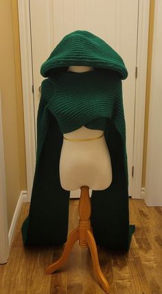 a mannequin wearing a green knitted shawl on top of a wooden stand