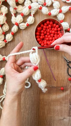 two hands are working with yarn and scissors on a wooden table next to some crochet