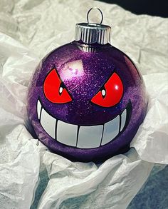 a purple ornament with red eyes and fangs on it's face is sitting on some white tissue paper