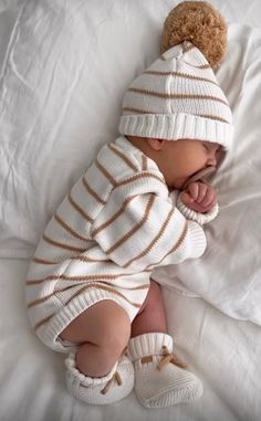 a baby wearing a white and brown striped outfit laying on top of a bed next to a teddy bear