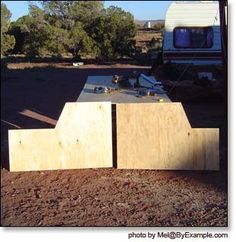 some wooden boards sitting in the dirt near a camper and trees, with a motor home in the background