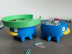 two blue and green plastic cups sitting on top of a table next to paper clips