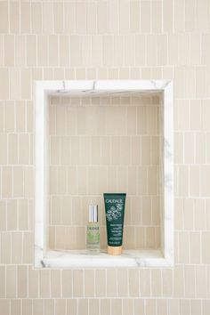 a white shelf with two bottles on it in a tiled wall area next to a toilet