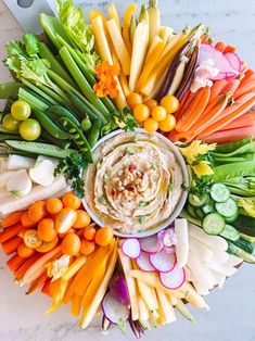 a platter filled with vegetables and dip surrounded by carrots, celery, radishes, cucumbers