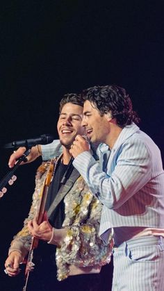 two men standing next to each other on stage with microphones in their hands and one man singing into the microphone