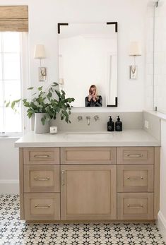 a woman taking a selfie in the mirror above a bathroom vanity with drawers and cabinets