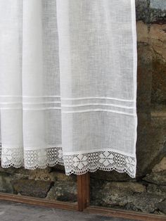 a white curtain is hanging on a wooden pole next to a stone wall and brick wall