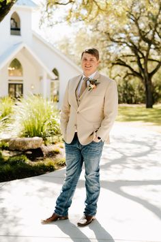 a man standing in front of a church wearing a tan suit and bow tie with his hands in his pockets