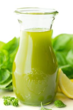 a glass bottle filled with green liquid next to lemons and greens on a white surface