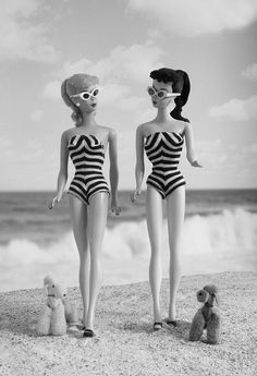 two dolls standing next to each other on the beach