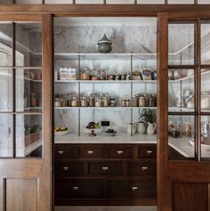 an open glass door leading to a kitchen with wooden cabinets and shelves filled with food