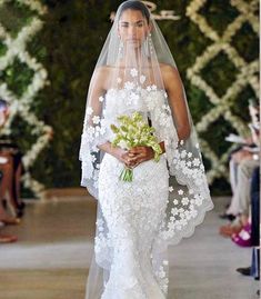 a woman in a white wedding dress holding a bouquet of flowers and wearing a veil