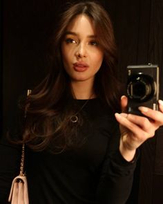 a woman taking a selfie in front of a mirror with her camera and handbag